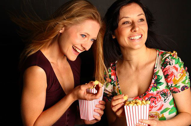Two girls eating popcorn while watching a movie